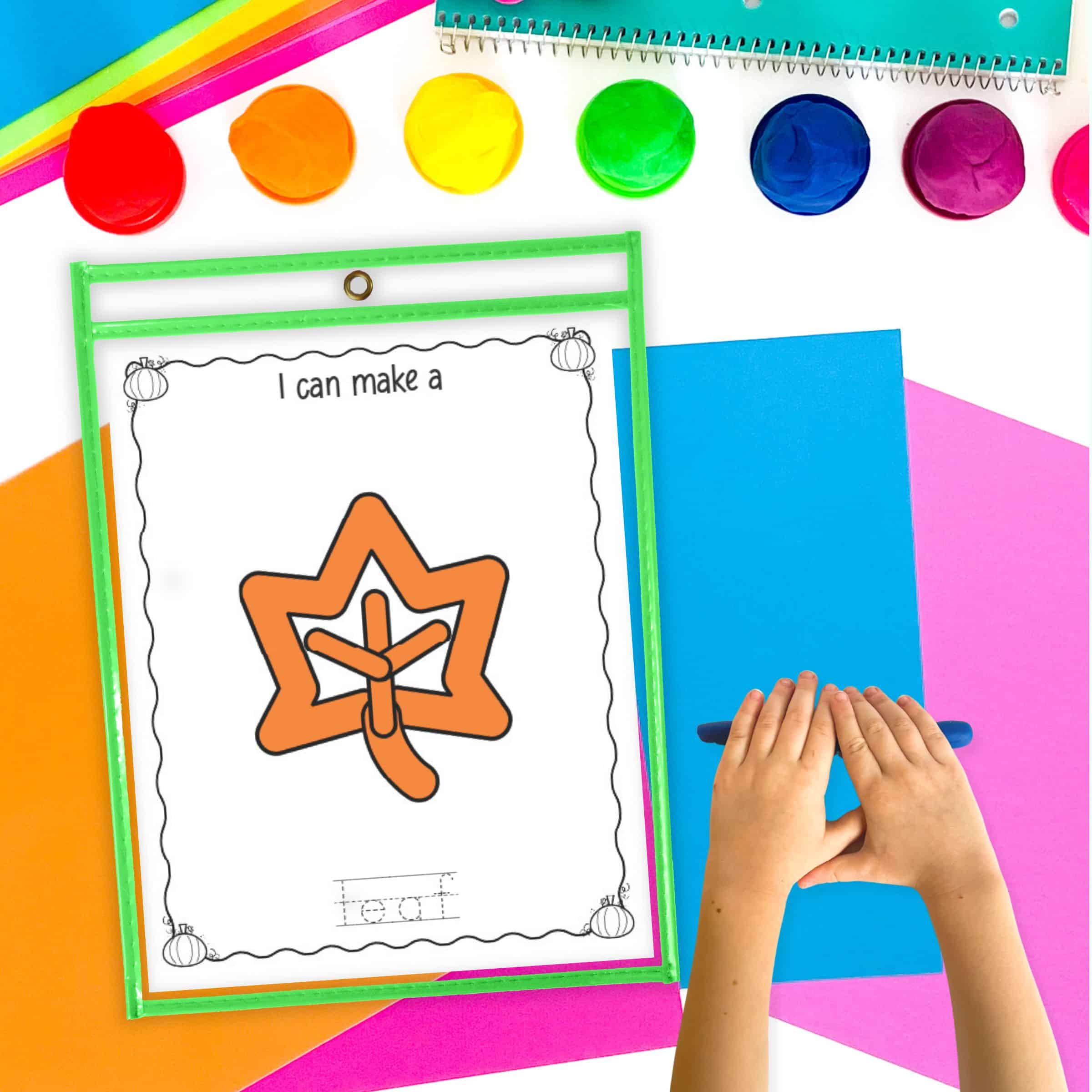 A leaf play dough mat in a dry erase pocket on a table with colorful papers and play dough