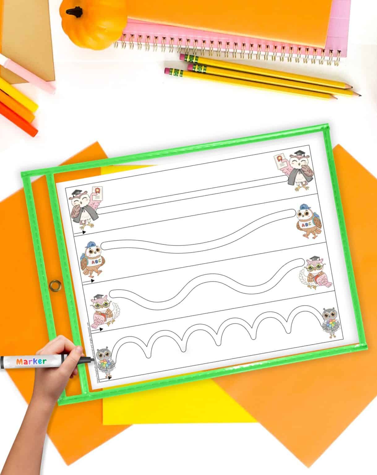 A top down image of an owl theme fine motor practice page with four paths to trace. The page is in ad ry erase pocket on a desk with fall colored school supplies