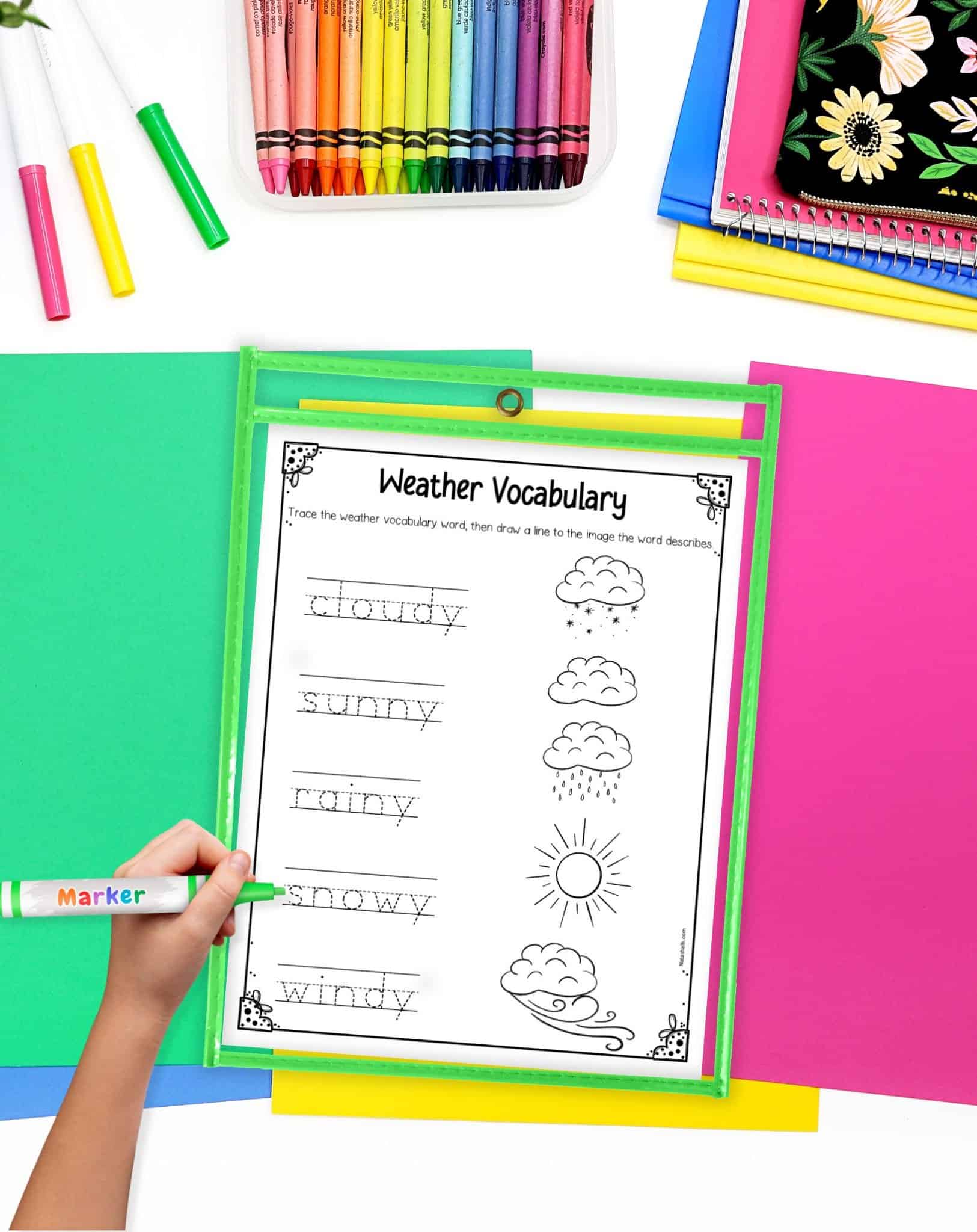 A worksheet with weather words to trace in a green dry erase pocket on a desk with colorful papers