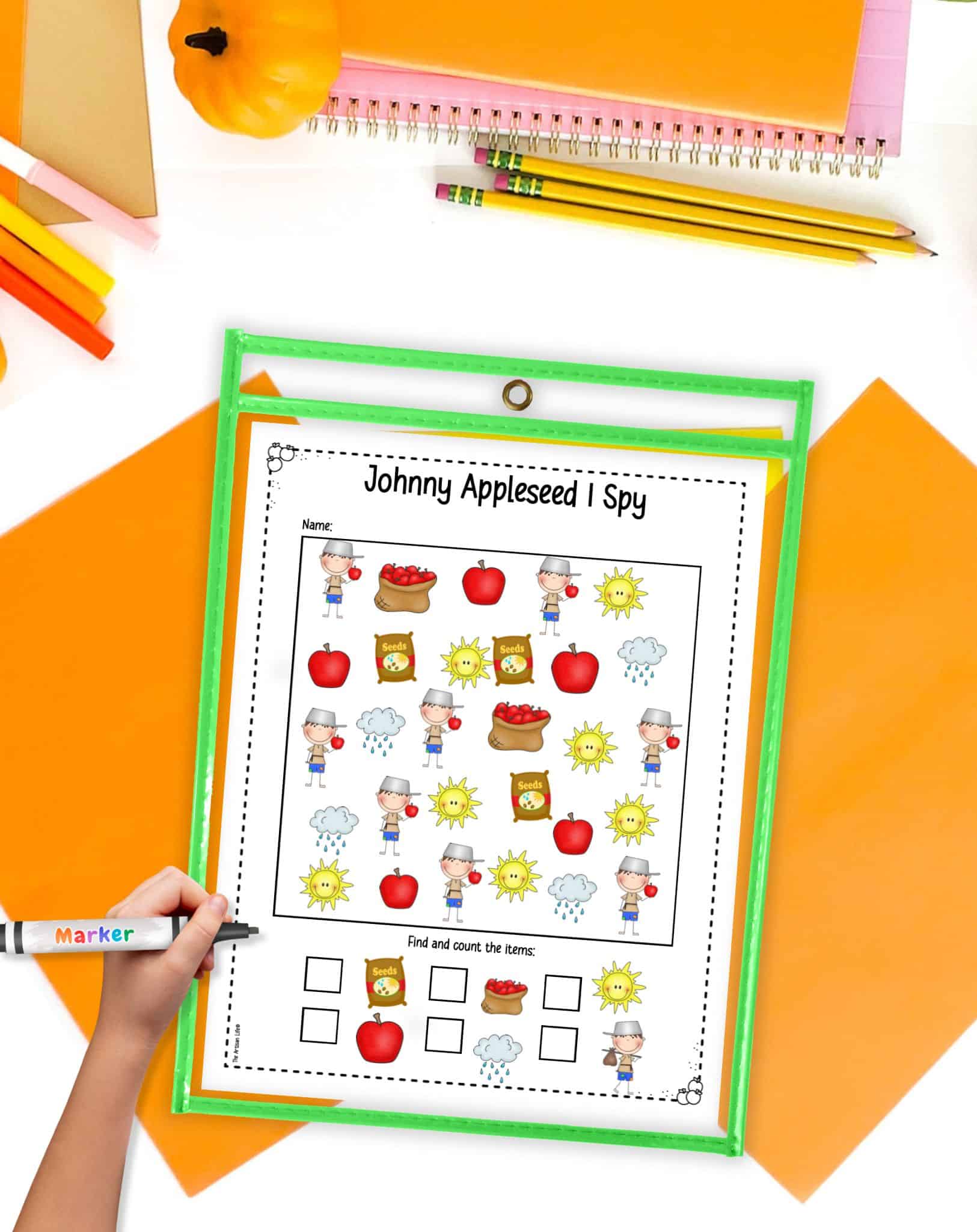 A Johnny Appleseed I Spy page in a dry erase pocket on a desk with orange papers and small pumpkins.