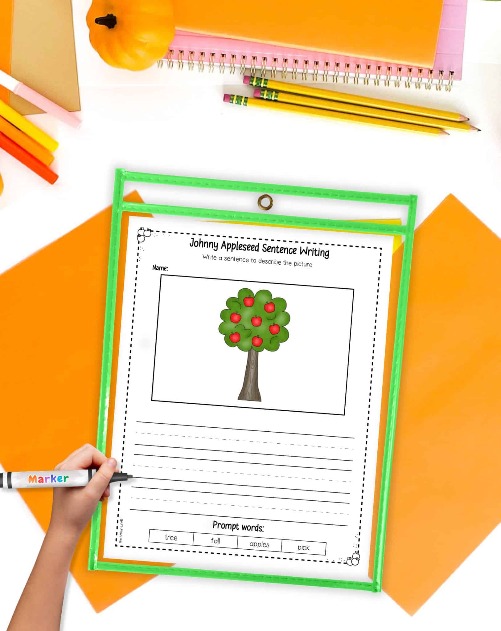 A top down view of a Johnny Appleseed writing prompt worksheet in a dry erase pocket on a table with orange papers and pencils