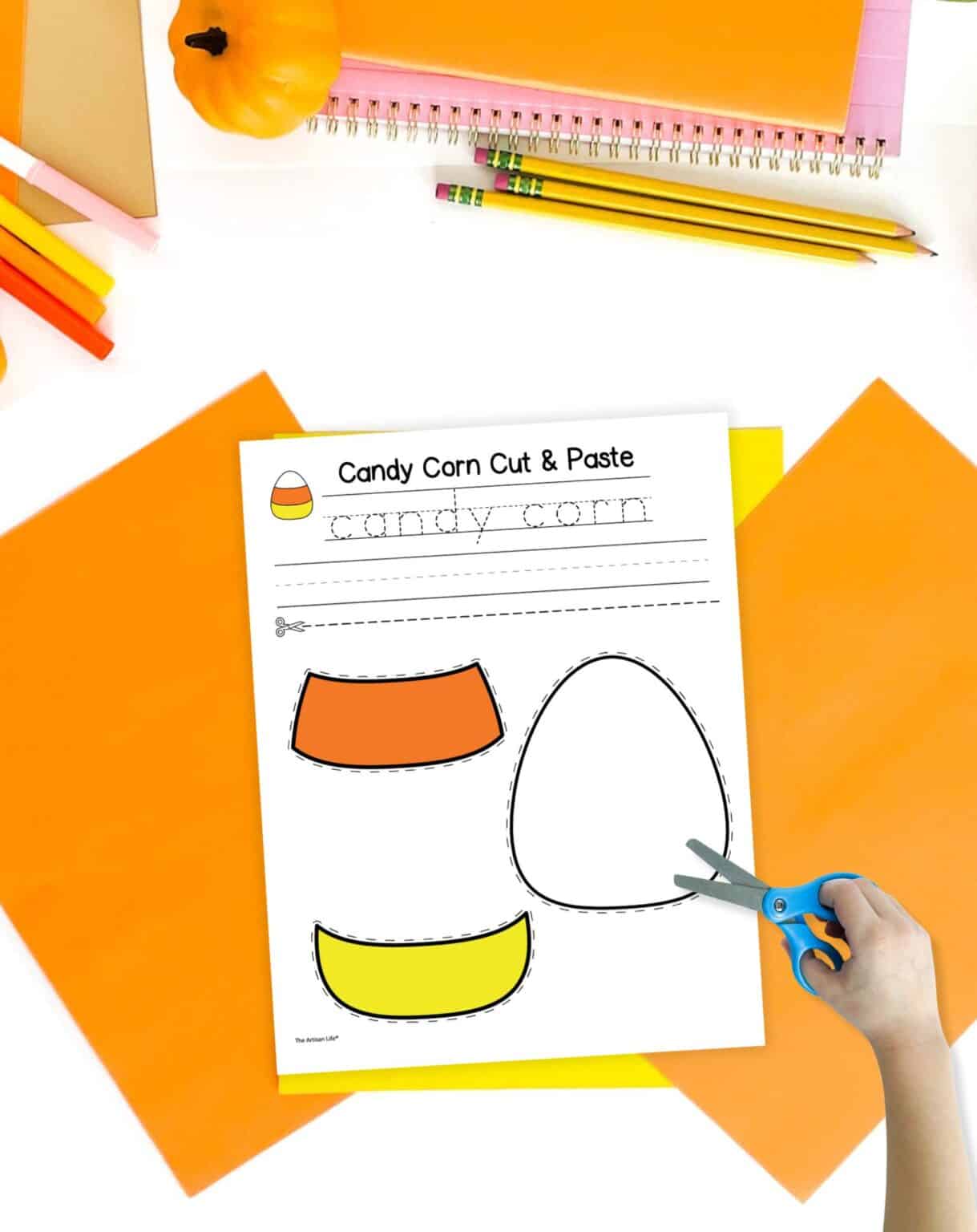 A candy corn cut and paste craft on a table with fall colored papers.