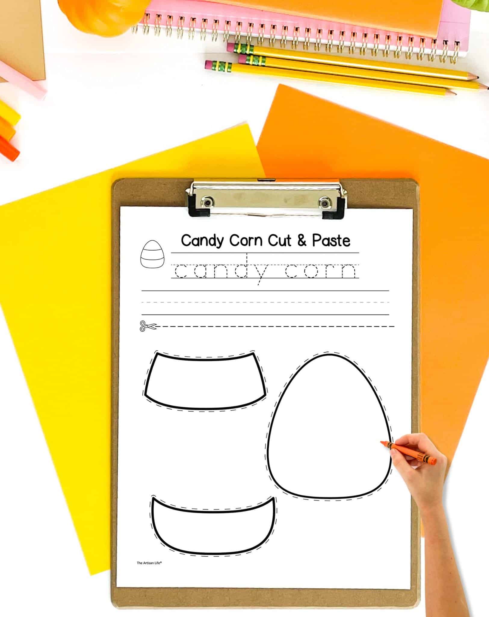 a black and white candy corn cut and paste craft on a clip board on a table with orange and yellow papers