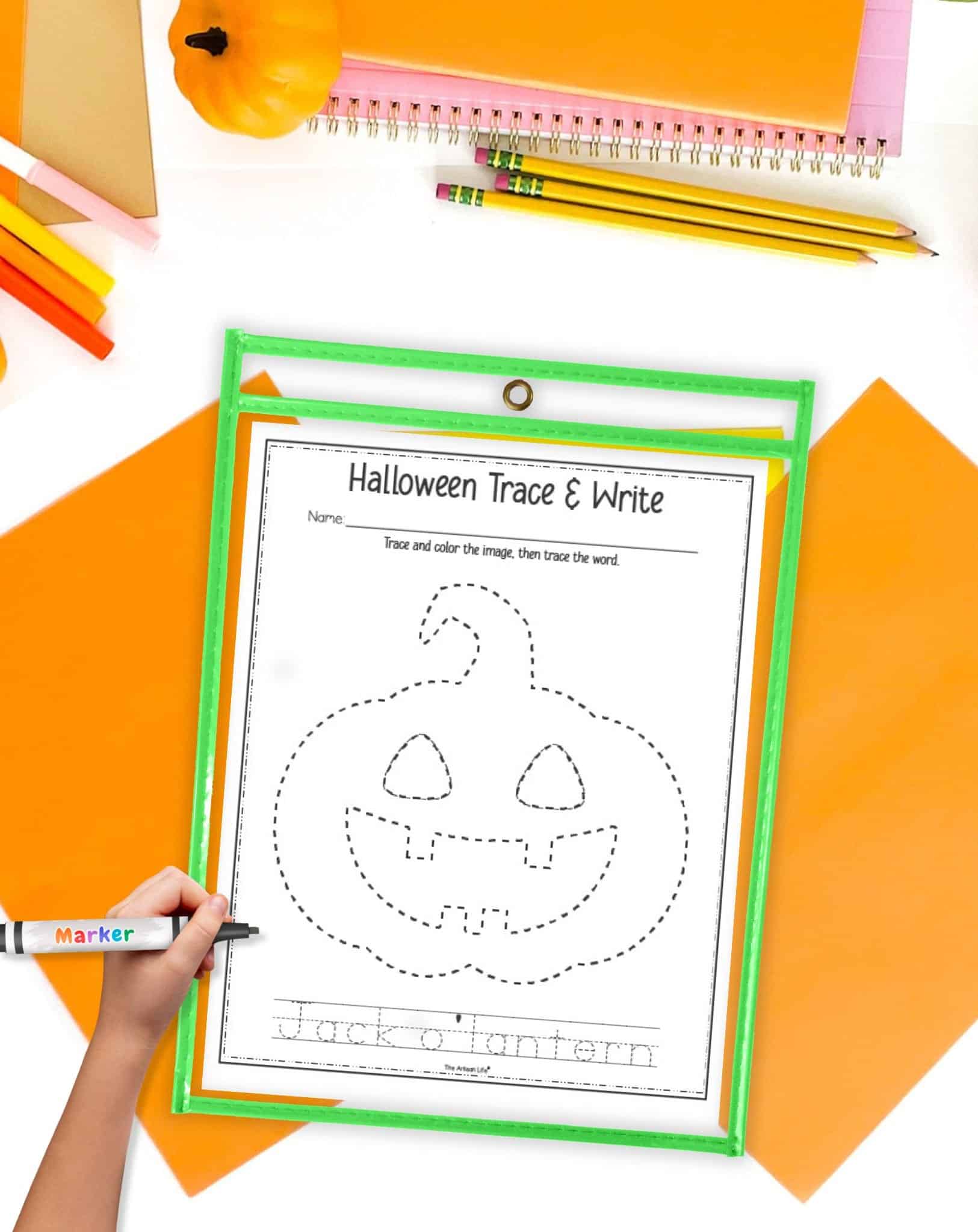 A jack o lantern tracing worksheet in a dry erase pocket on a table with orange papers and pencils