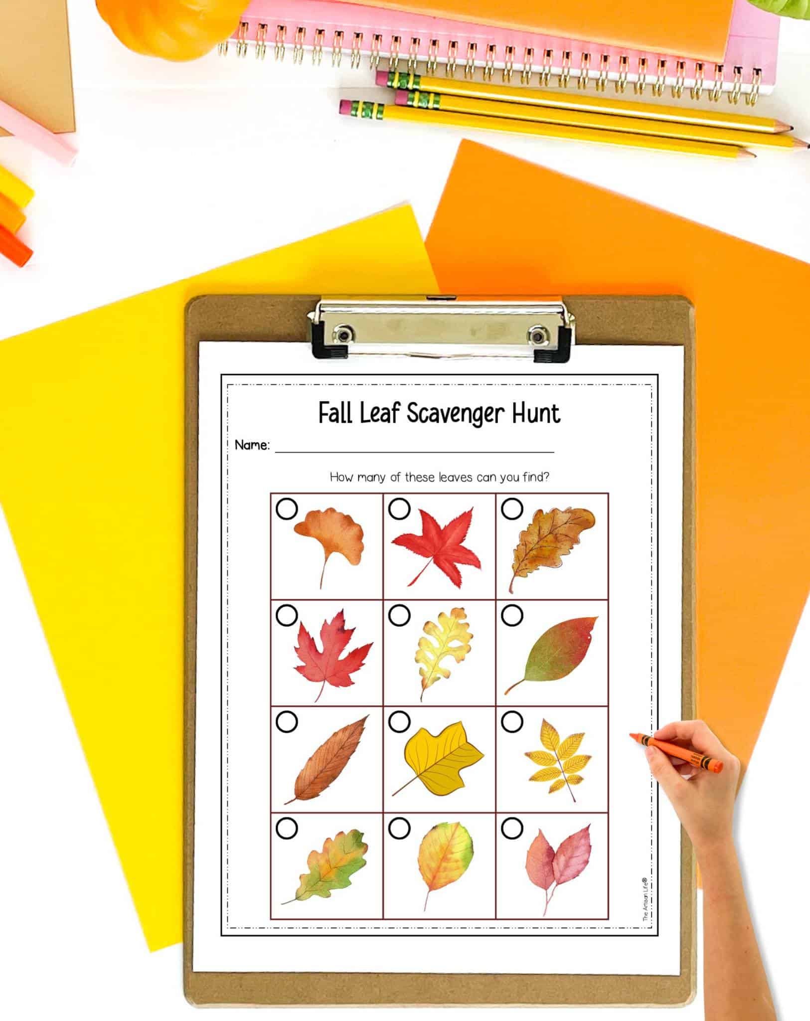 A fall leaf scavenger hunt for kids on a clip board. A hand holding a crayon is visible in the foreground.