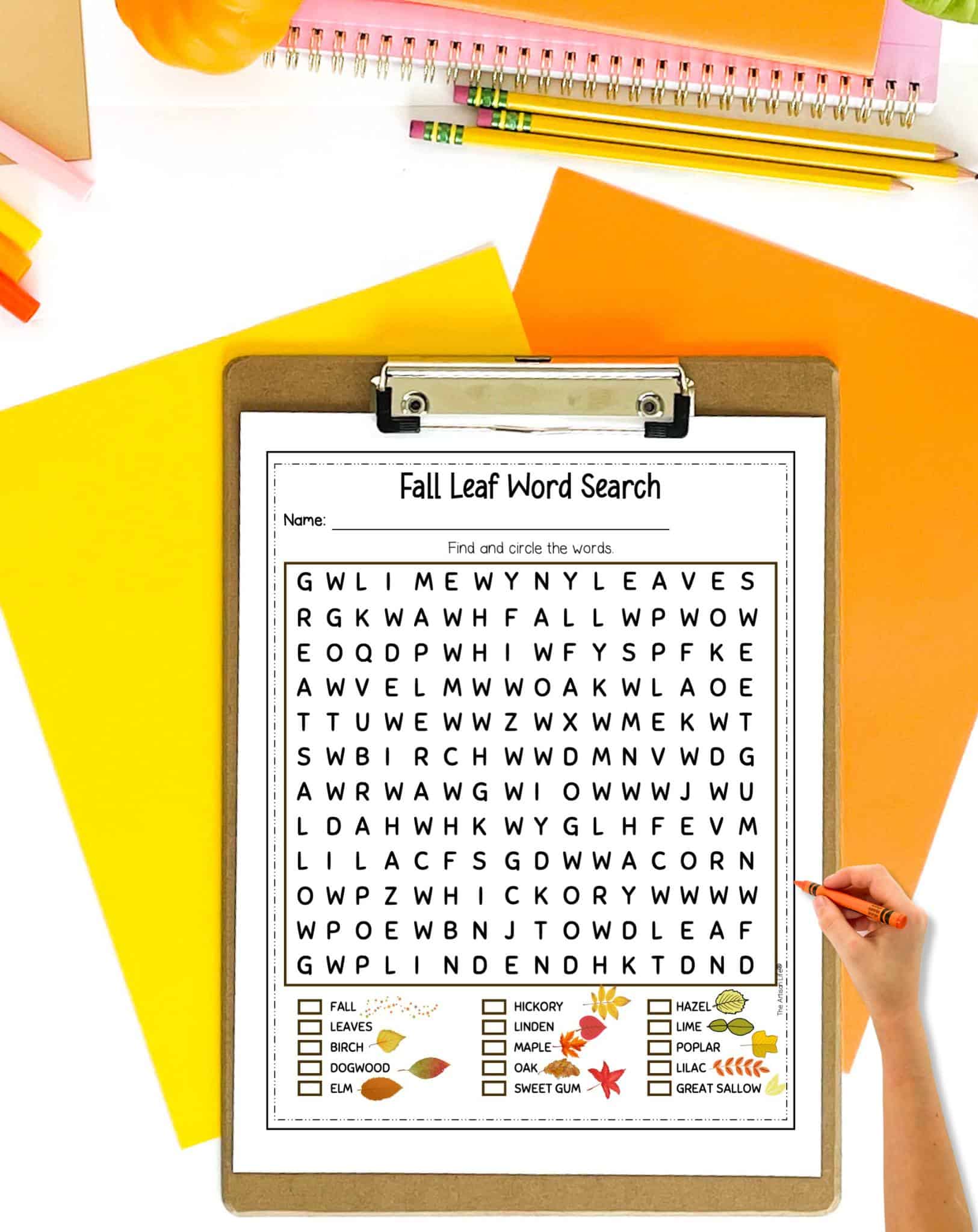 A fall leaf word search on a clip board. The clip board is on a table with yellow and orange papers and pencils.