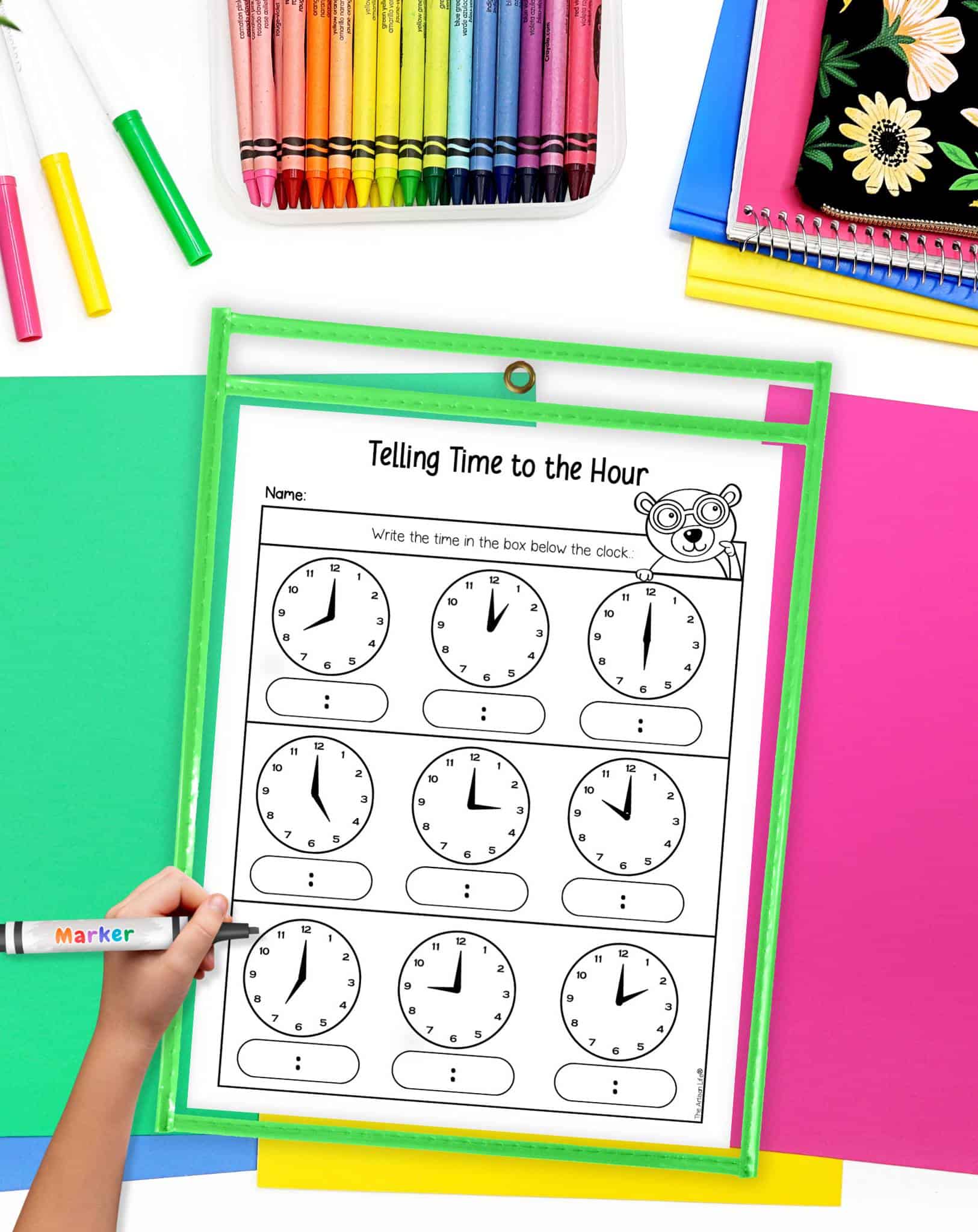 A time telling to the hour worksheet in ad ry erase pocket on a desk with colorful papers