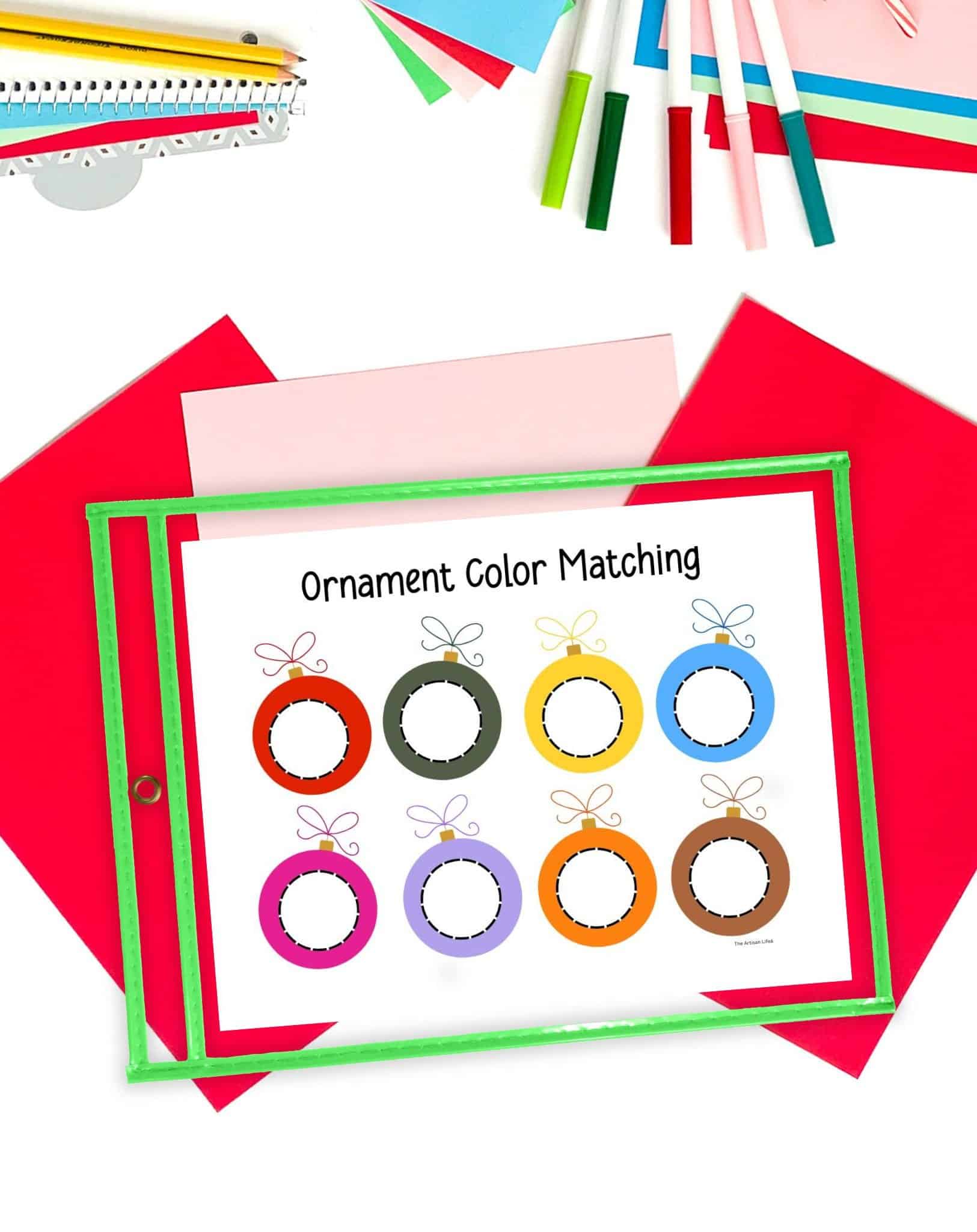 a Christmas ornament color matching activity in ad ry erase pocket on a desk with Christmas stationary items