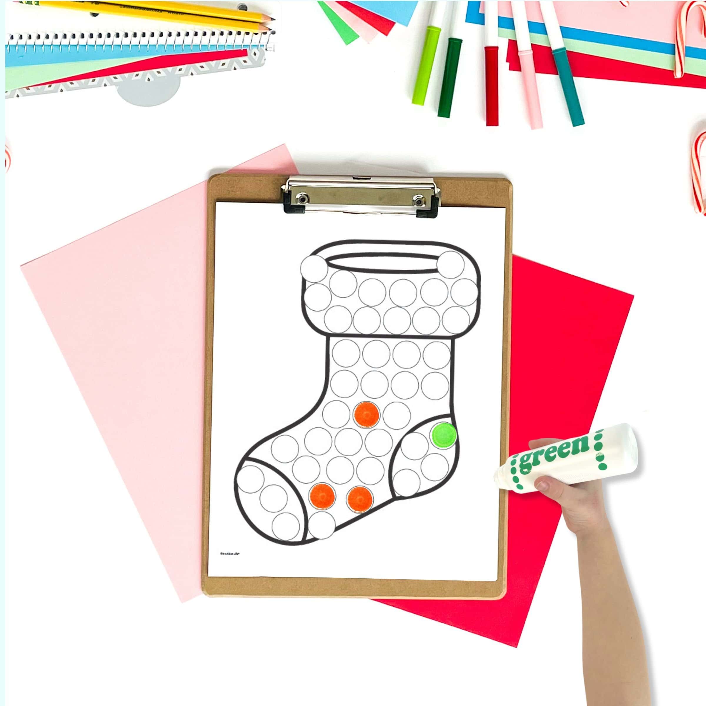 A dot marker page of a stocking on a clipboard with colorful christmas papers and markers