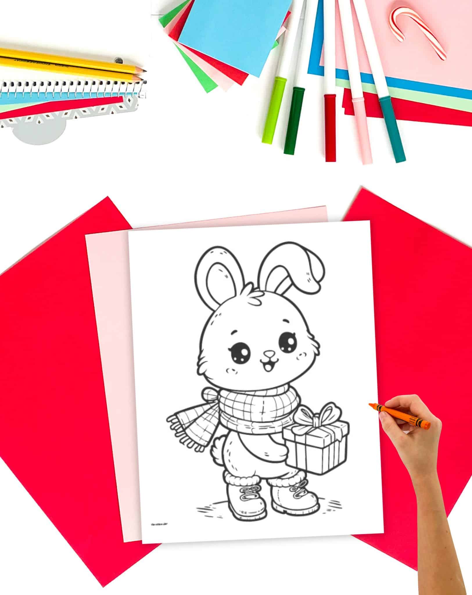 A coloring page showing a bunny holding a present on a desk with colorful christmas supplies