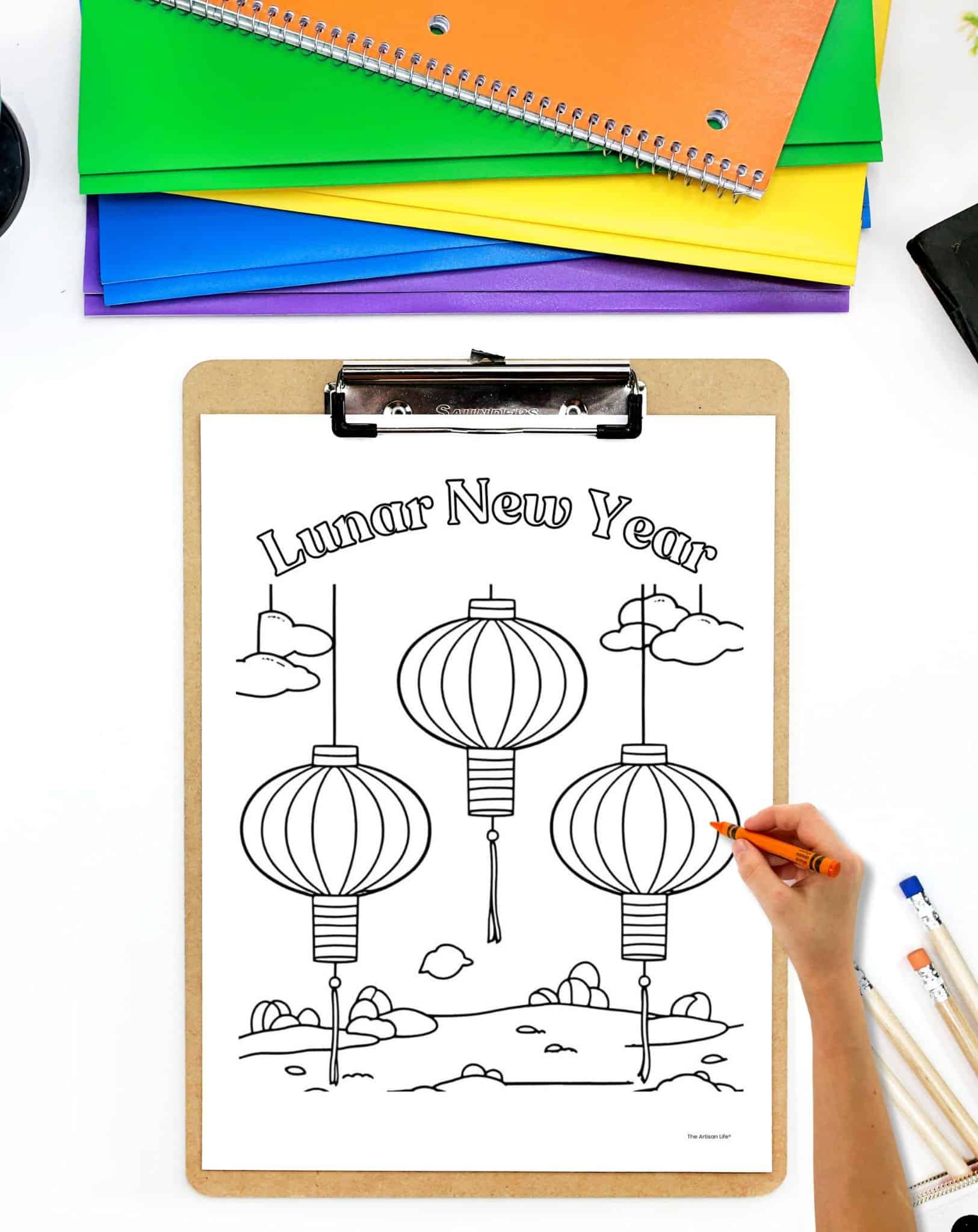 a coloring page with the text "lunar new year" and three paper lanterns on a clipboard. A child's hand holding an orange crayon is visible in the foreground