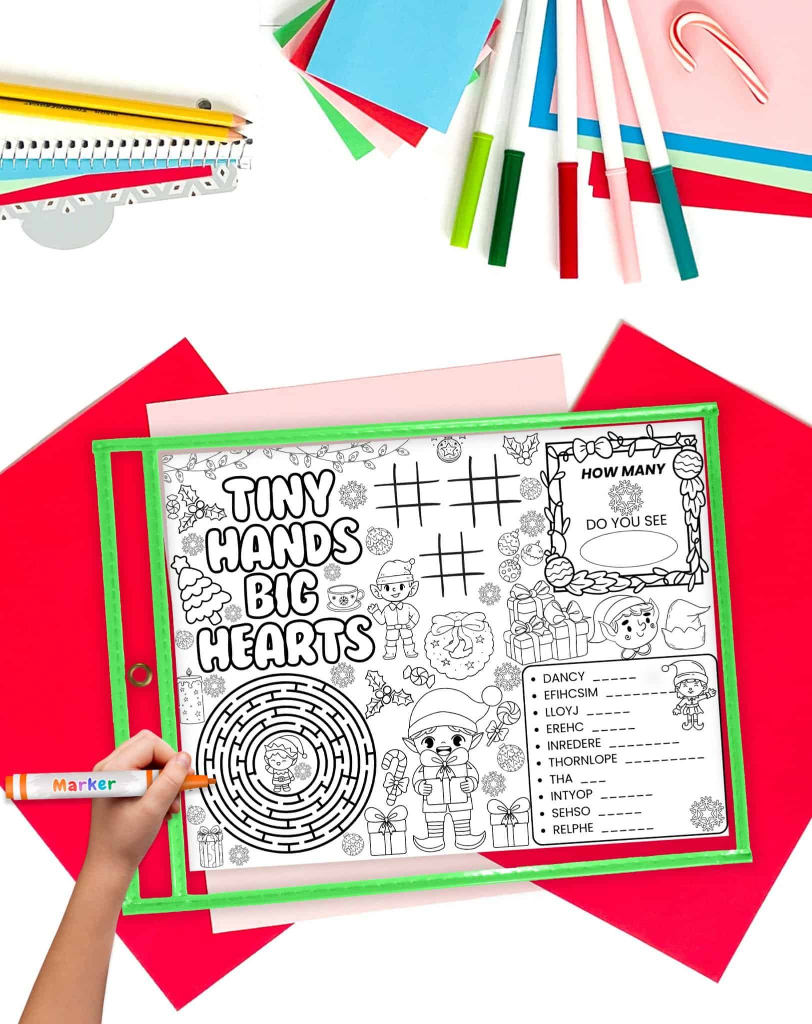 A christmas elf activity placemat in a green dry erase pocket. A hand holding a marker is visible in the foreground. 