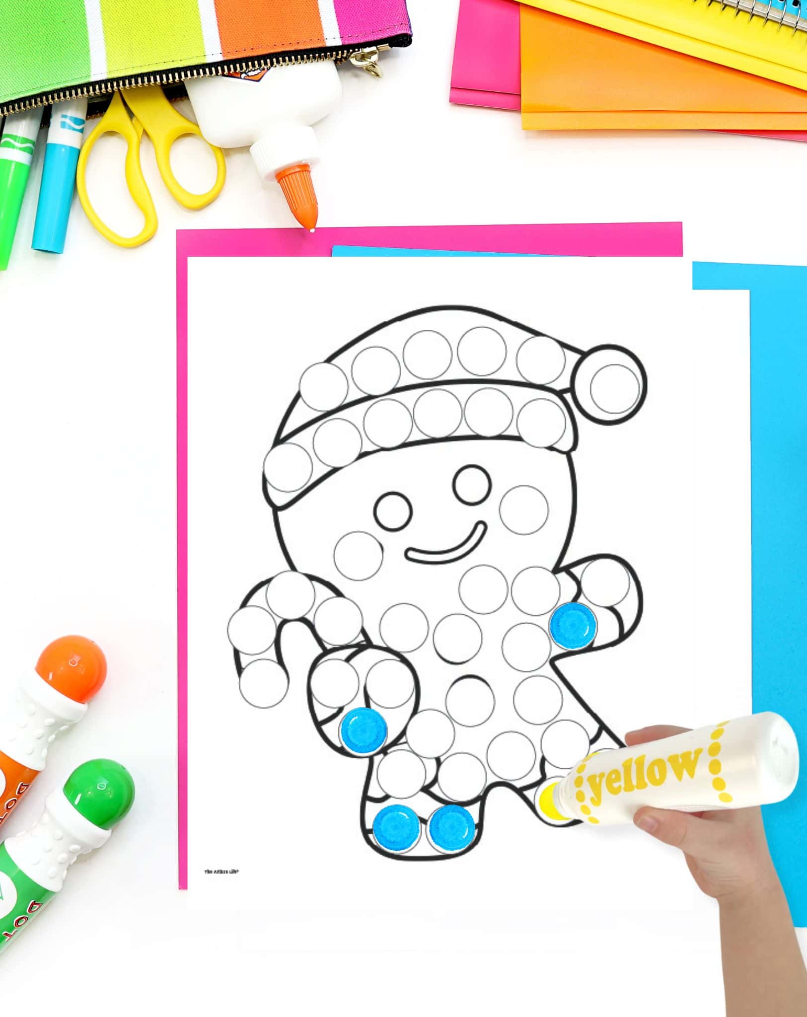 a partially completed gingerbread man dot marker coloring page. A child's hand holding a dauber marker is visible in the foreground. 