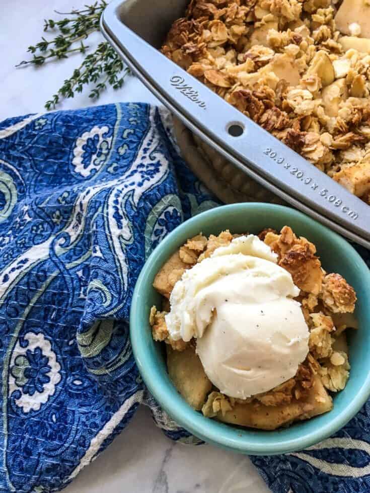 a vertical image of baked apple crisp in a bowl with ice cream on top