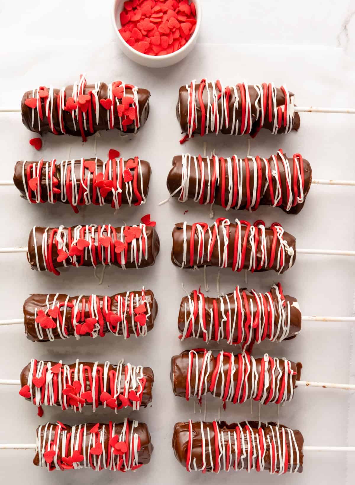 red and white chocolate on marshmallow pops with red heart sprinkles being added