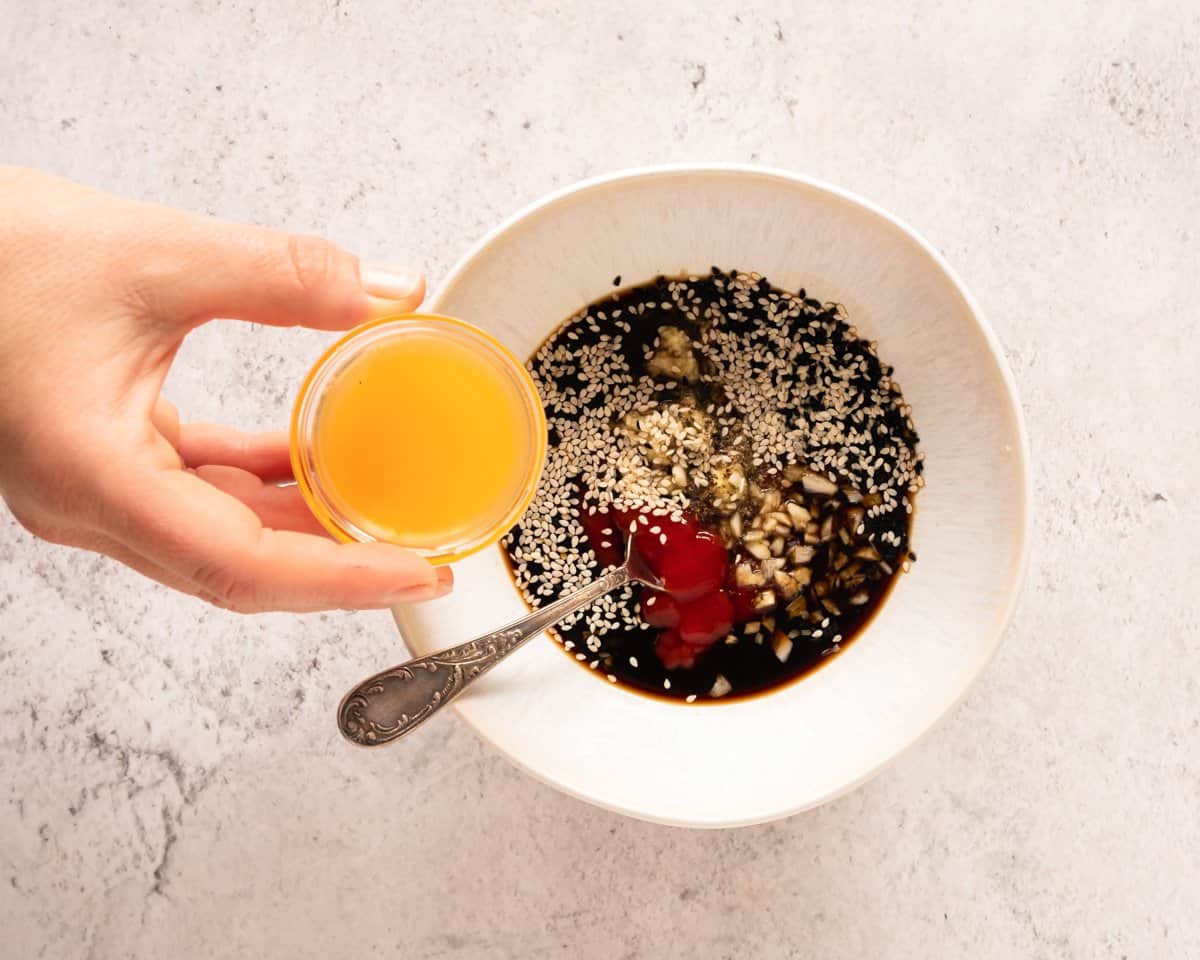 adding honey to a bowl with soy sauce and sesame seeds to make a sauce for chicken 