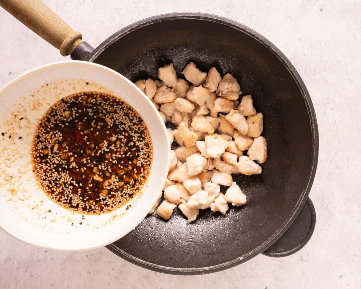 adding sauce with sesame seeds to a skillet with cooked pieces of chicken 