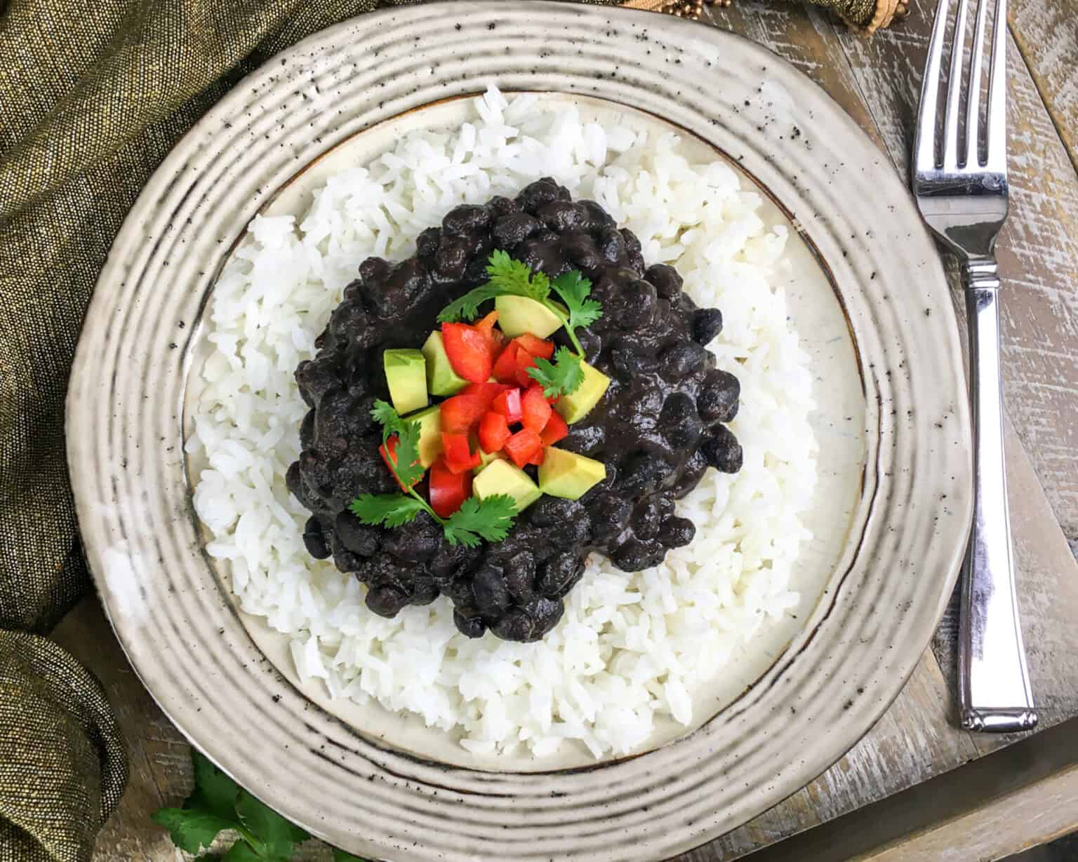 a plate with white rice, black beans, and red pepper and avocado on top