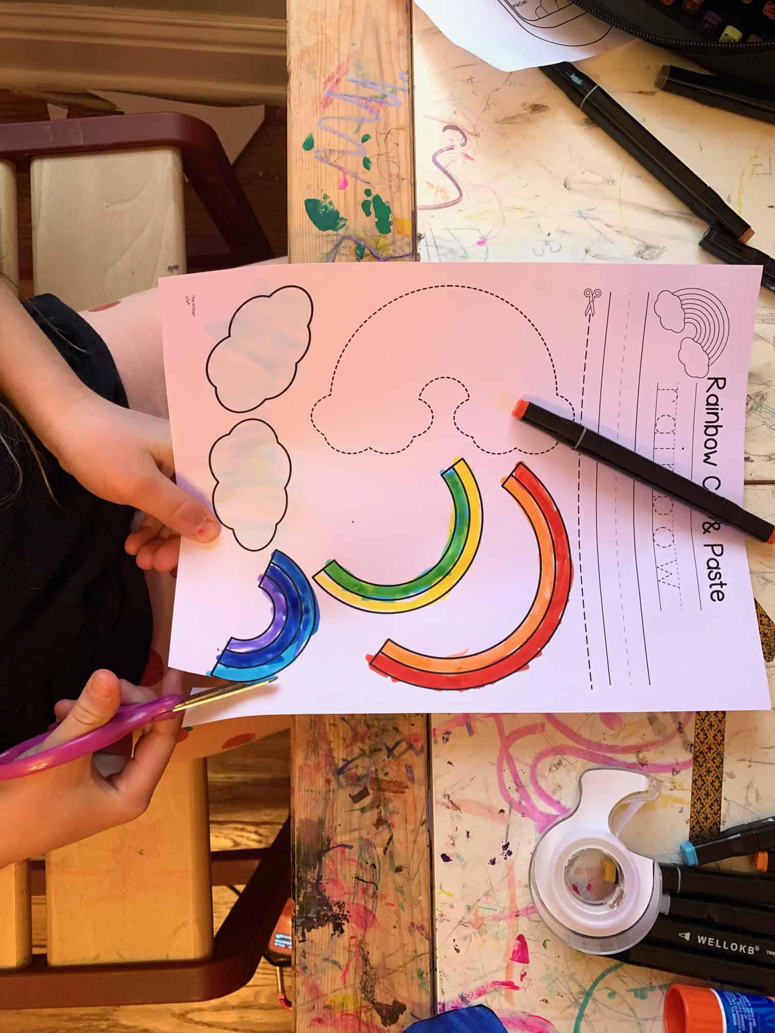 a child cutting out a colored rainbow cut and pate craft at a child's desk