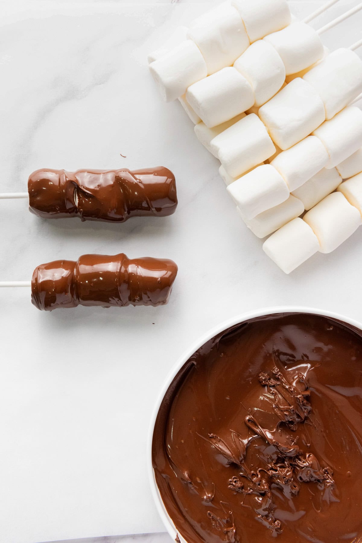 lollipop sticks with marshmallows and a bowl of melted chocolate