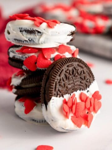 a photo of white chocolate dipped Oreos with red heart sprinkles