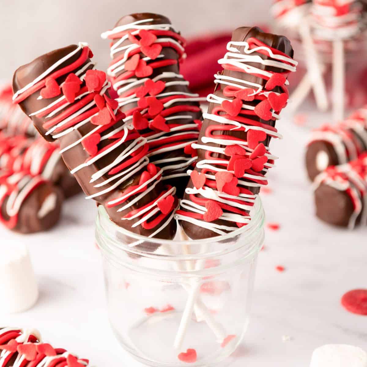 a jar with three completed Valentine's marshmallow pops with red and white chocolate and red heart sprinkles 