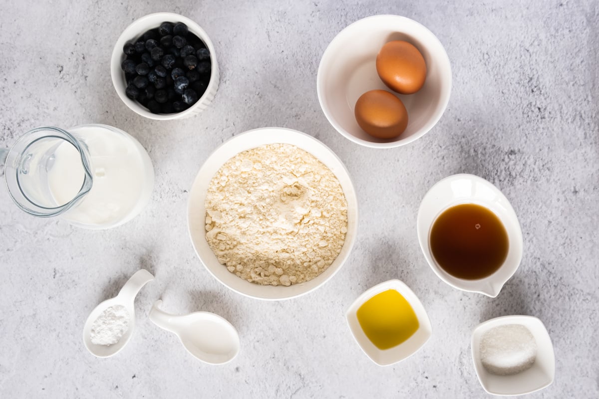 ingredients for gluten free pancakes including milk, eggs, blueberries, and gluten free flour