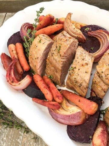 a sliced honey and orange glazed pork roast on a white serving dish with roasted vegetables