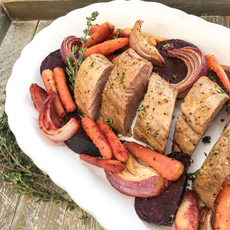 a sliced honey and orange glazed pork roast on a white serving dish with roasted vegetables