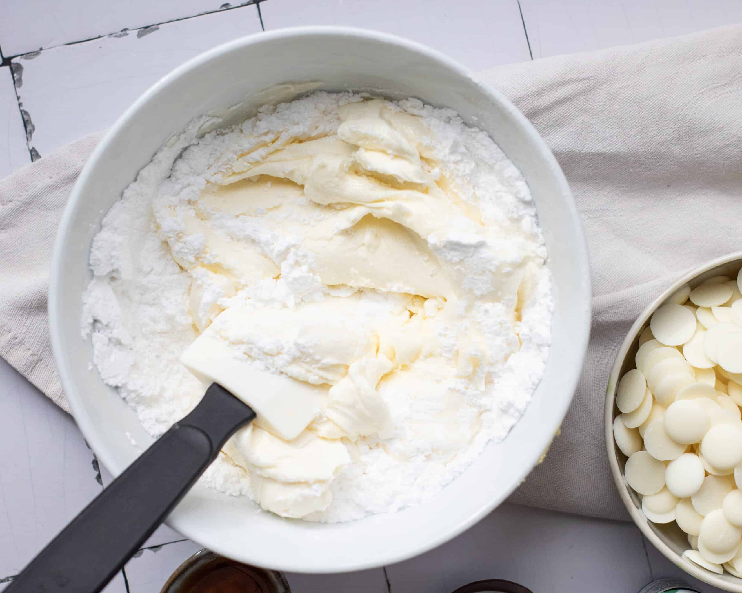 a bowl with cream cheese and powdered sugar being mixed with a spatula 