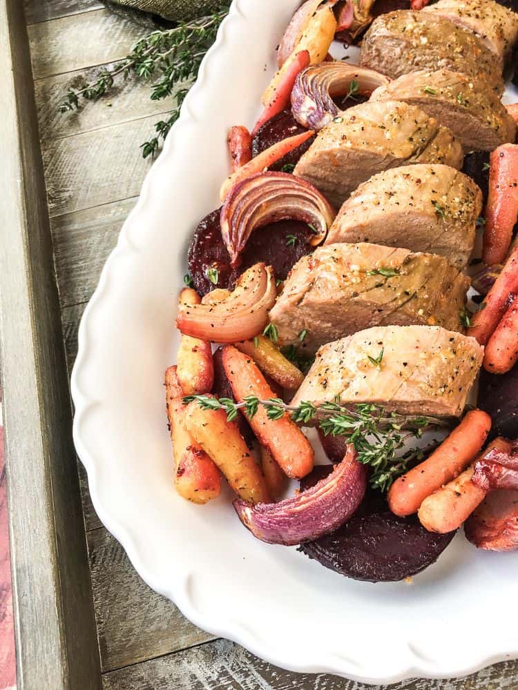 a white platter with sliced roasted pork loin and roasted colorful root veggies