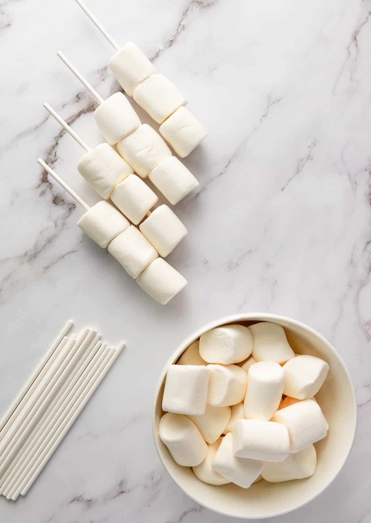 a top down photo with a bowl of marshmallows and popsicle sticks