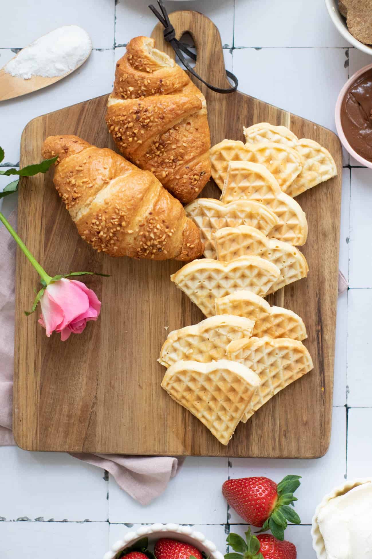 Heart shaped waffles and croissants on a cutting board with a rose