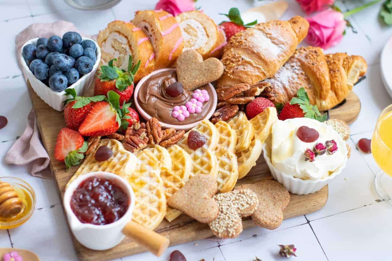 a photo of a family breakfast board for Valentine's Day with heart shaped waffles, fresh fruit, and pastries