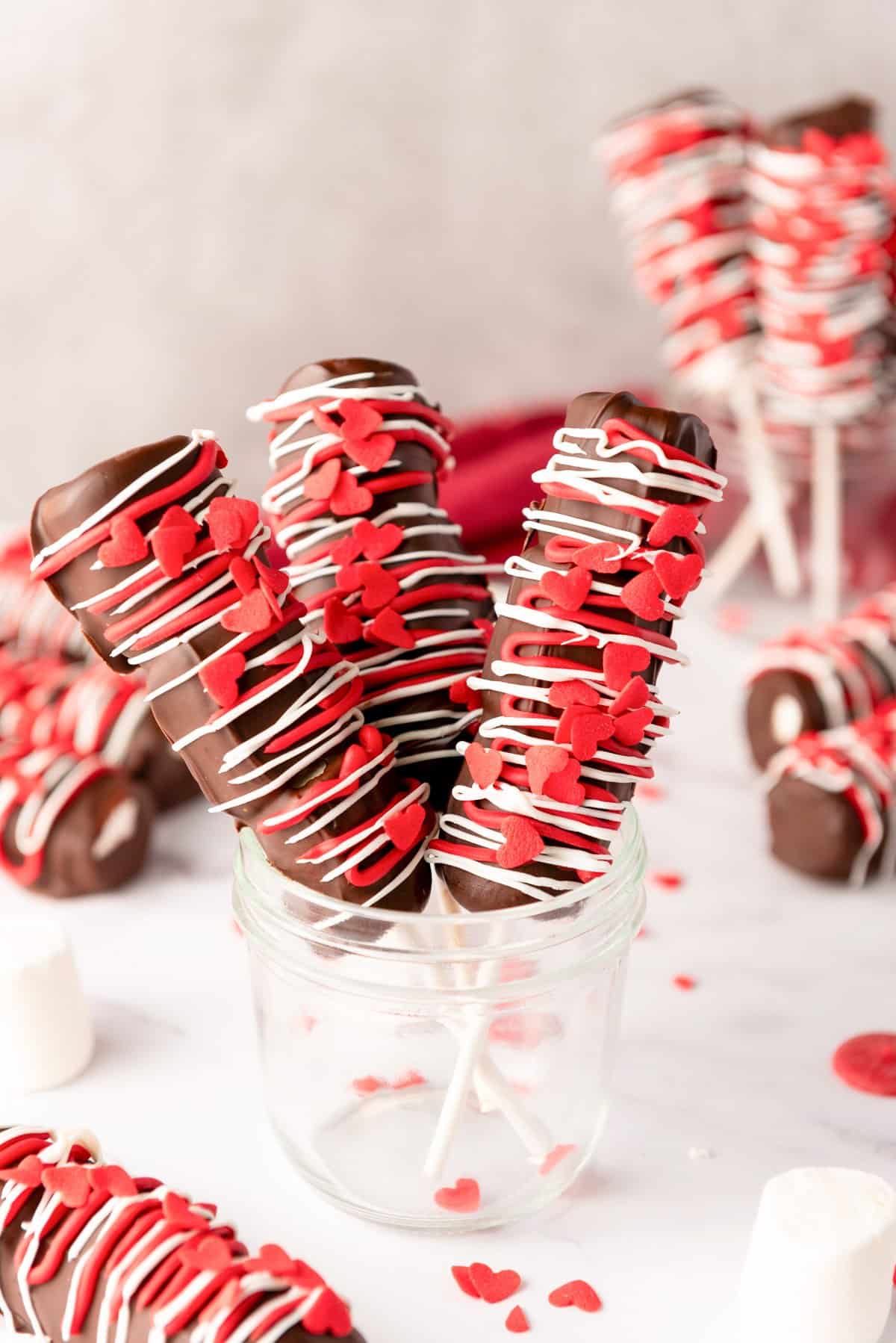 a jar with three completed Valentine's marshmallow pops with red and white chocolate and red heart sprinkles 