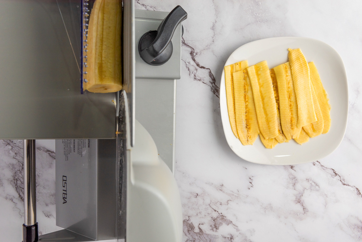 plantain being sliced on a mandolin slicer