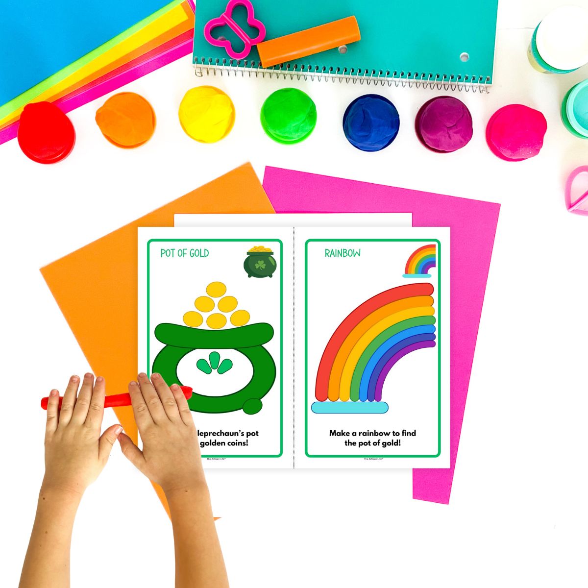 A hand holding red playdough is positioned above two printable playdough mats featuring activities themed around an Irish flag and a lucky horseshoe, surrounded by various colored playdough and construction paper.
