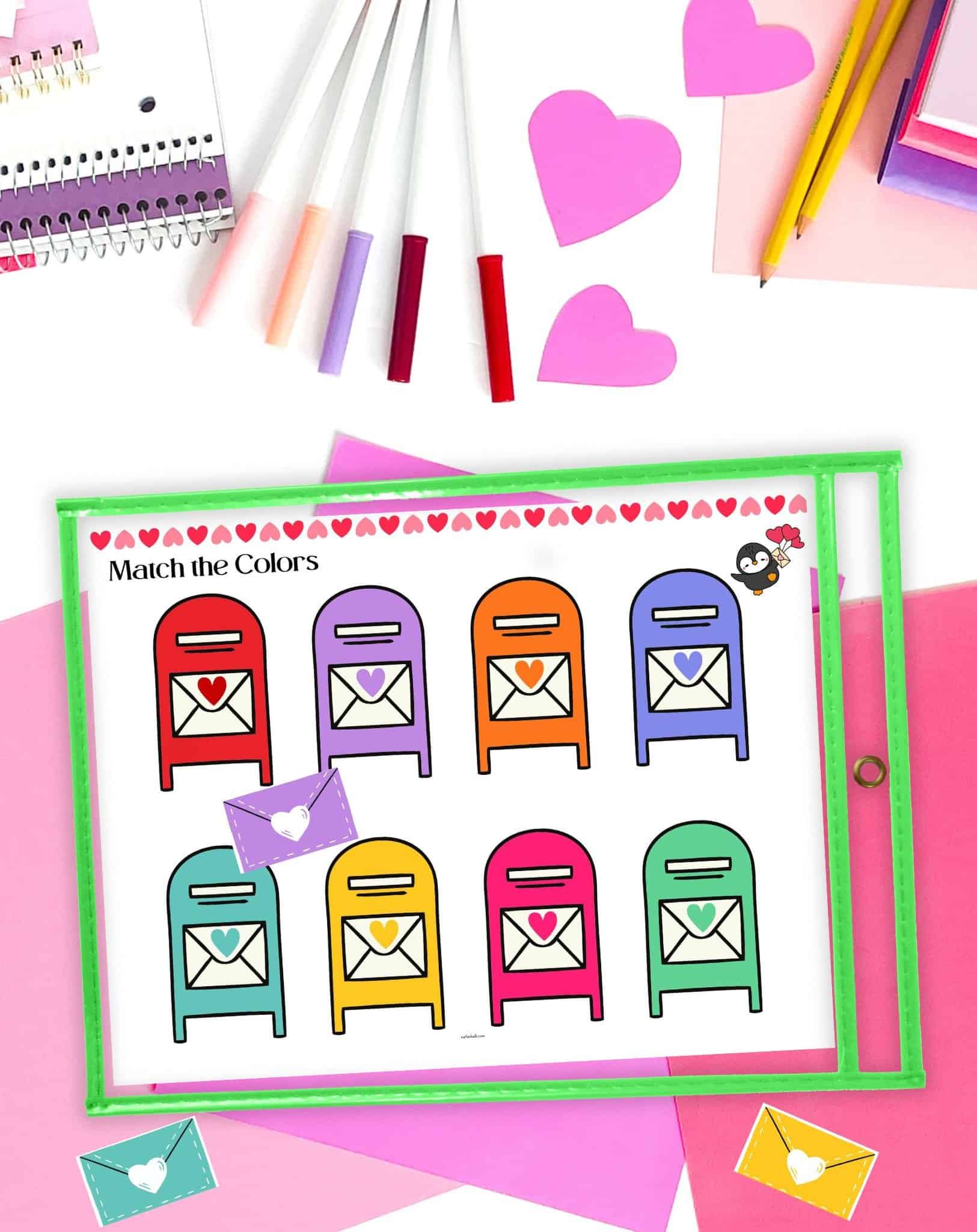 a color matching activity for Valentine's Day in a dry erase pocket on a table with pink stationary supplies