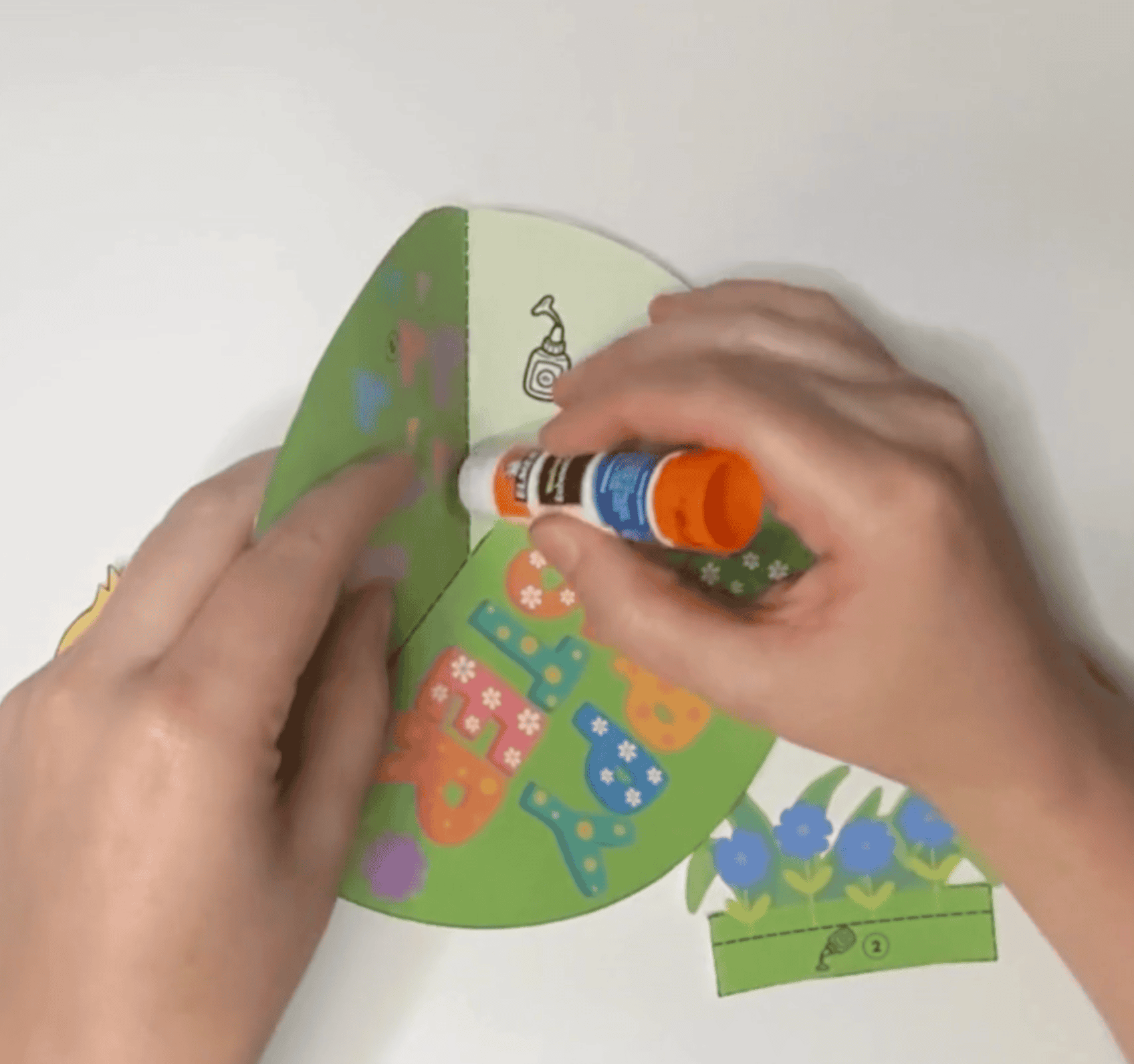 A person is assembling a DIY printable Easter card for kids by applying glue to colorful cut-out shapes, illustrating a spring craft activity suitable for preschoolers and kindergarteners.
