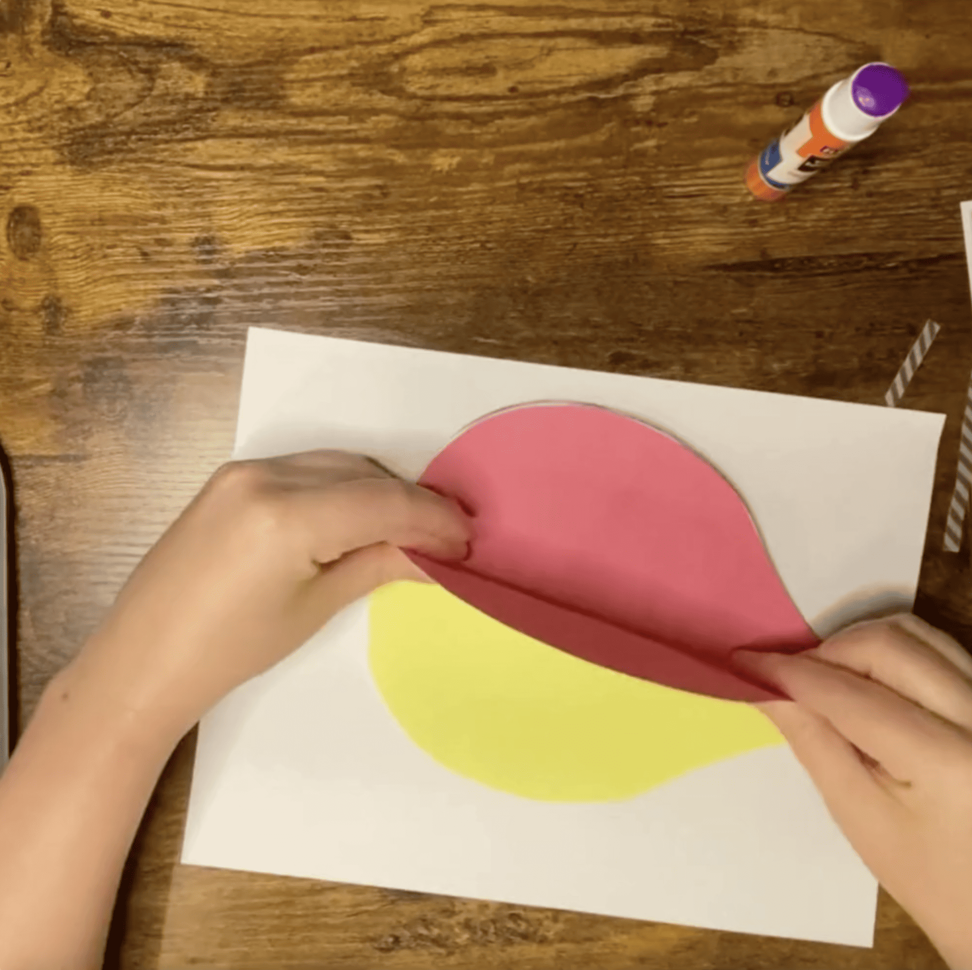 A person's hands are seen arranging cut paper shapes on a larger sheet, likely as part of a hot air balloon craft project for preschool, using paper templates suitable for various balloon-themed art activities.
