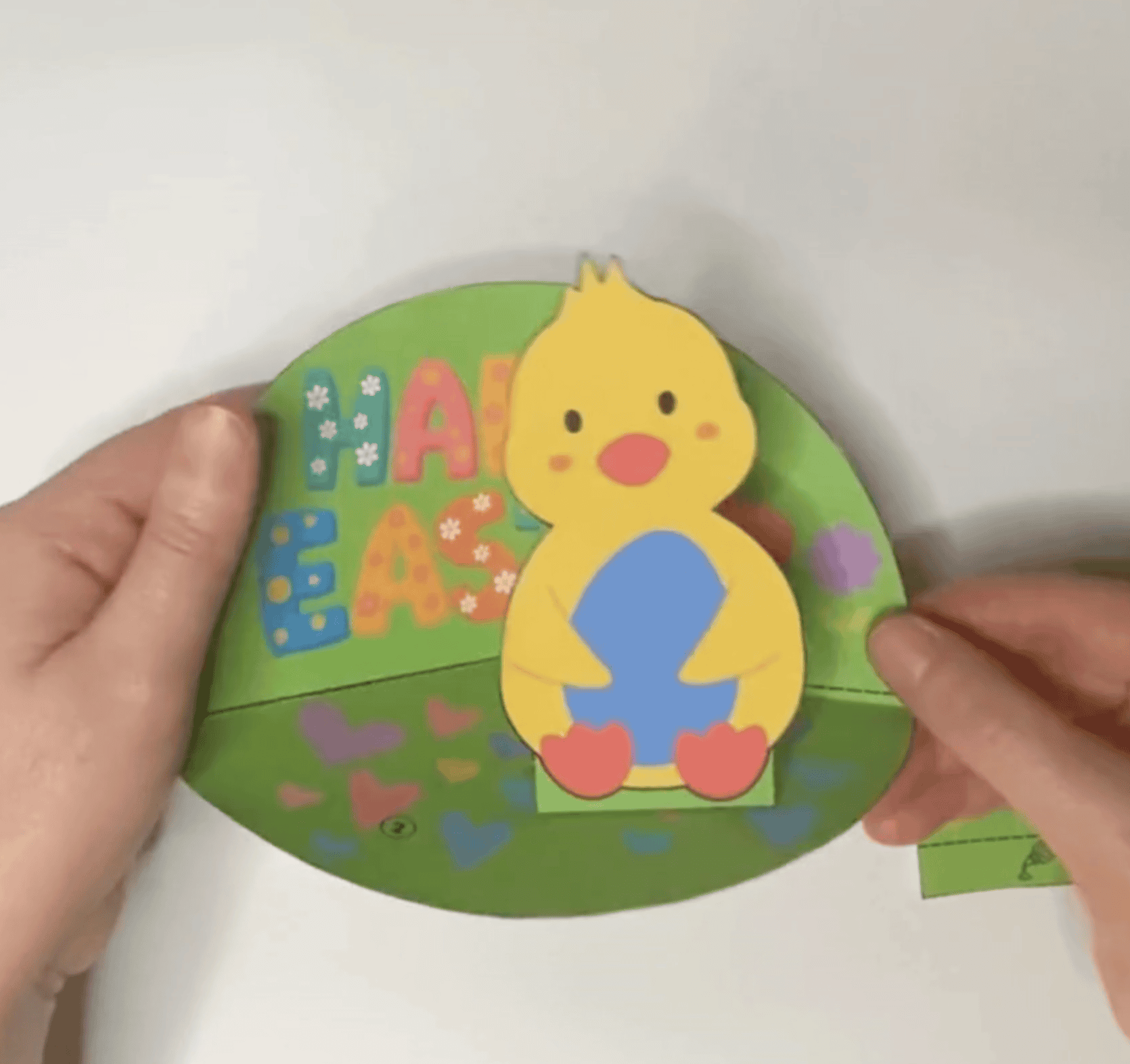 A pair of hands holds a colorful DIY Easter card that reads "Happy Easter" with a chick and flower design, suitable for kids' spring crafts and printable activities.
