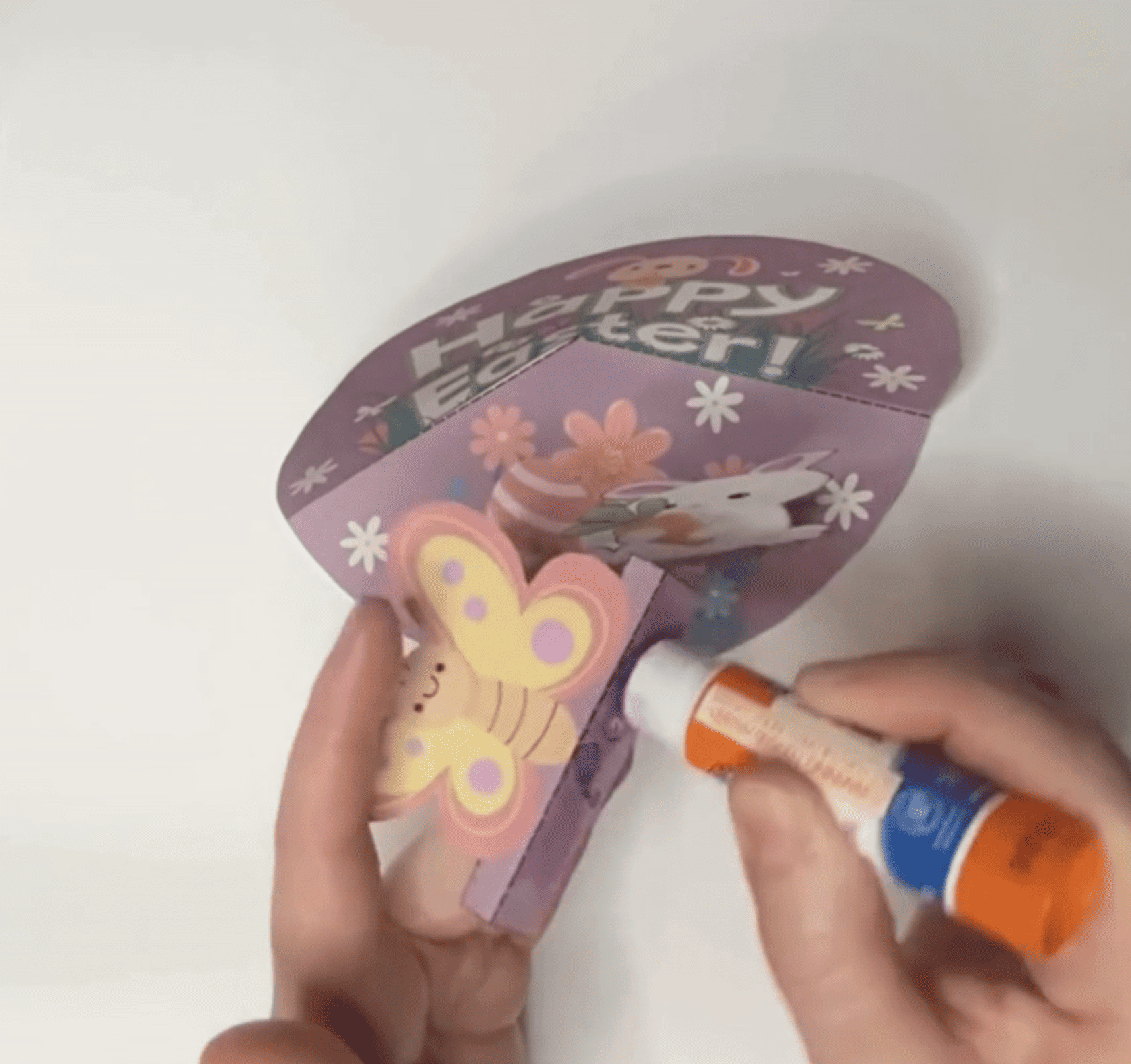 A person is applying glue to create a DIY Easter card featuring a butterfly design, intended for kids' spring crafts, which may include free printable Easter activities and crafts for preschool or kindergarten.
