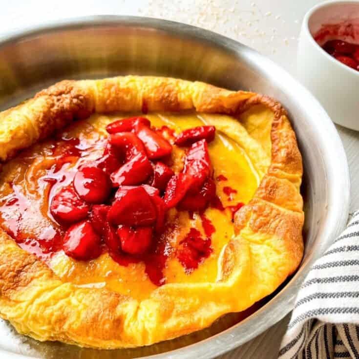 a Dutch baby pancake topped with strawberries in a stainless skillet.