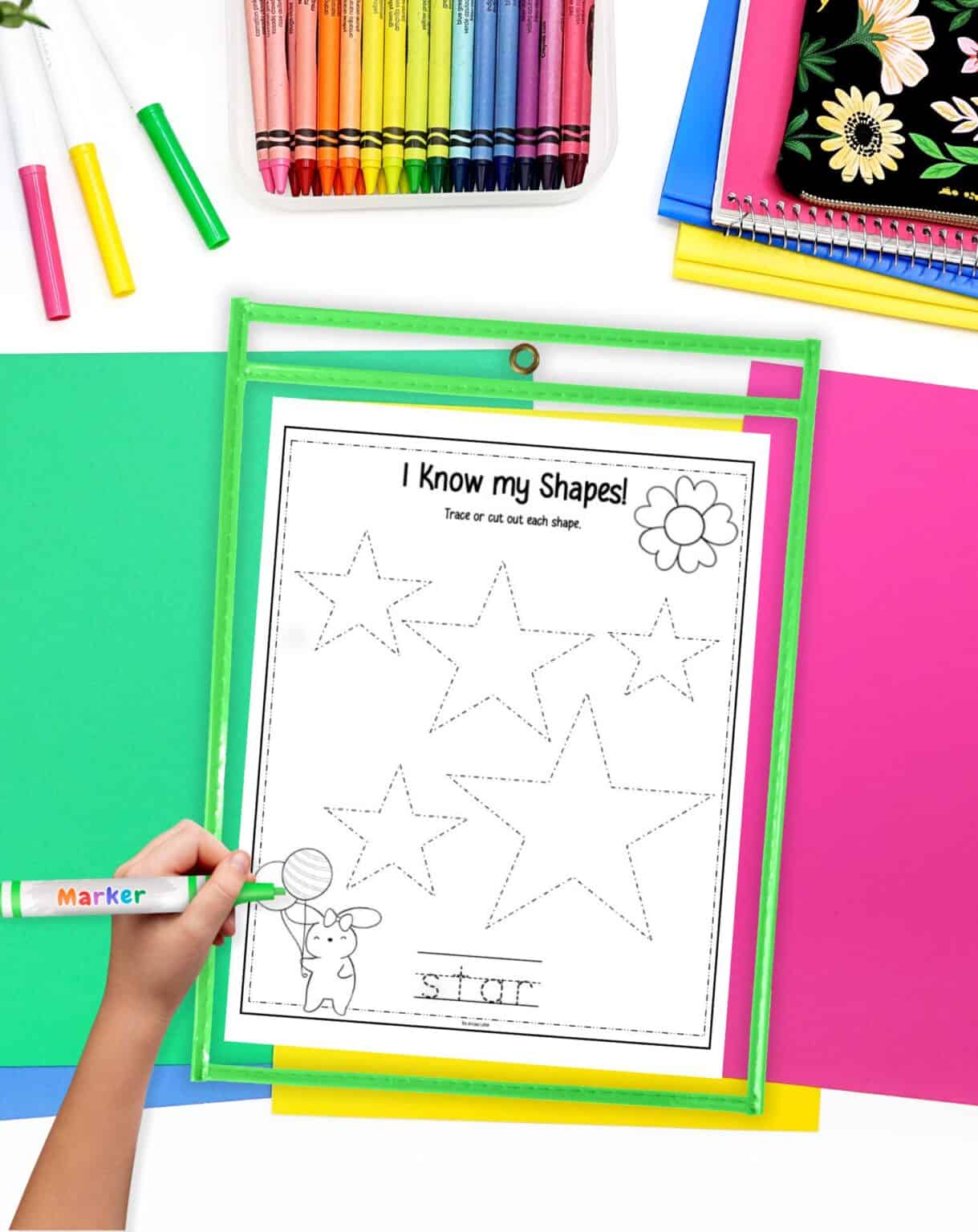 A hand holding a marker traces shapes on a worksheet titled "I Know my Shapes!" surrounded by colorful construction paper, highlighting Easter-themed learning activities for preschoolers.