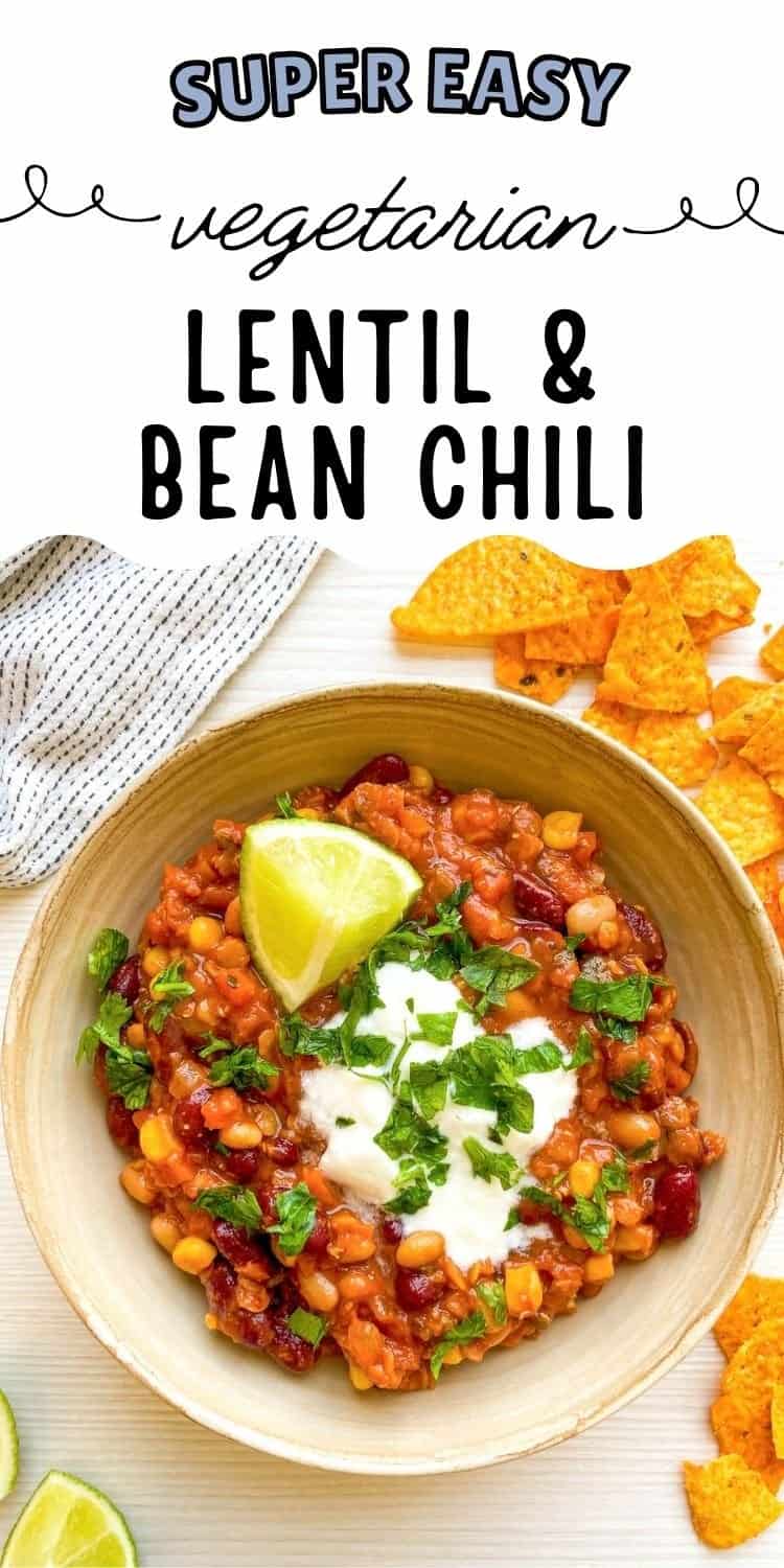 A bowl of vegetarian chili featuring a mix of beans, topped with sour cream, chopped cilantro, and a lime wedge, served alongside tortilla chips.
