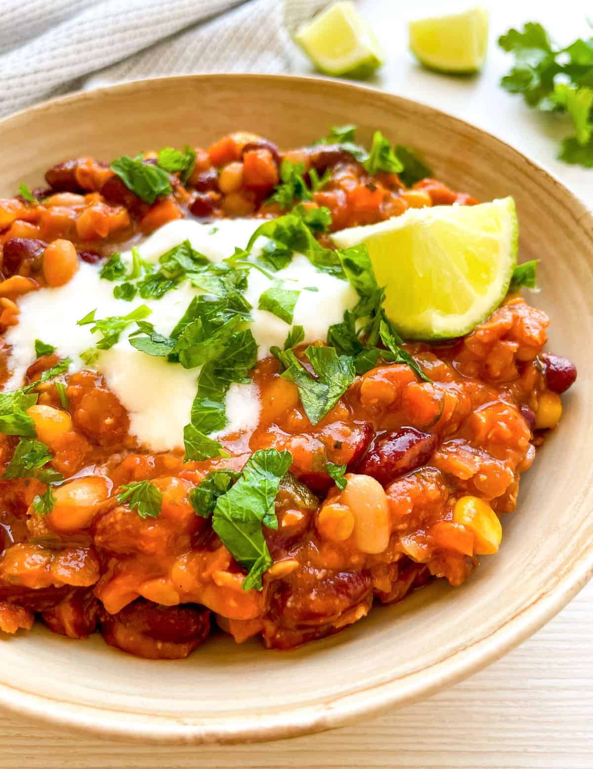 A bowl of vegetarian chili topped with sour cream, lime, and chopped cilantro, accompanied by tortilla chips, showcases an easy vegetarian chili recipe rich in beans and corn, ideal for nutritious dinners or filling lunches.
