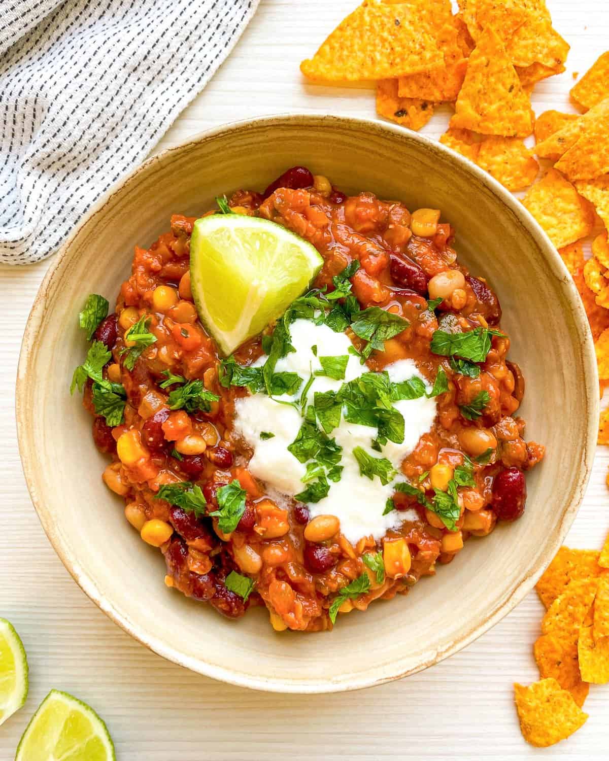 A bowl of vegetarian chili topped with lime, herbs, and yogurt is served alongside tortilla chips, illustrating an easy vegetarian chili recipe perfect for nutritious dinners or filling lunches.

