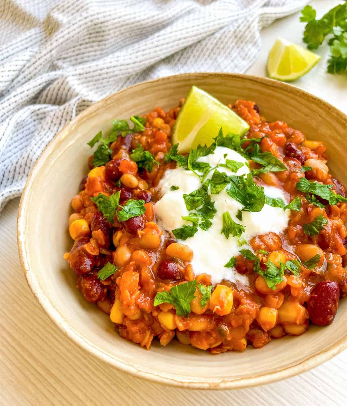 A bowl of colorful vegetarian chili topped with sour cream, cilantro, and lime, served with tortilla chips, featuring a hearty mix of beans and corn for a nutritious and filling meal.
