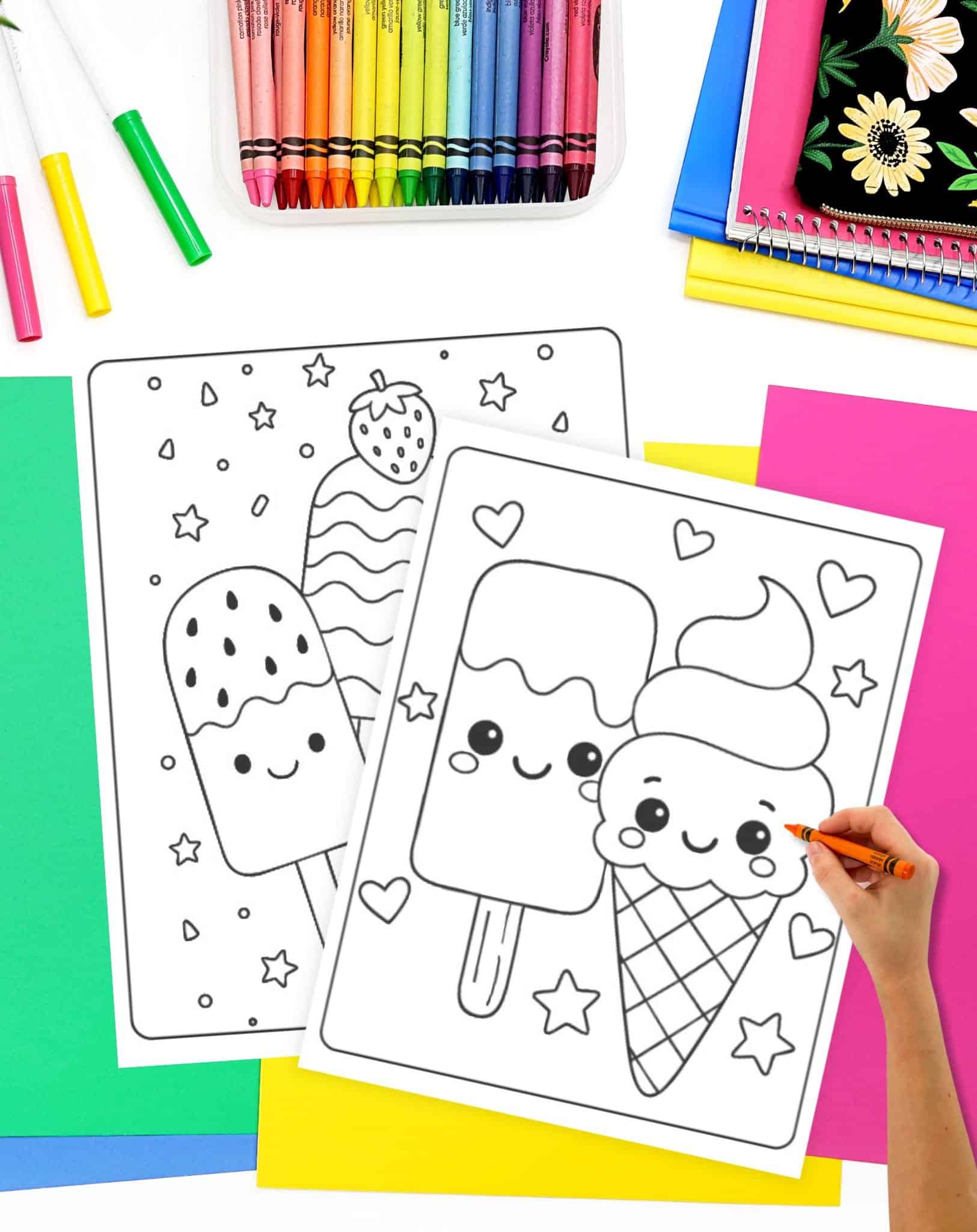 A hand colors in a kawaii popsicle and ice cream cone on summer-themed coloring pages, surrounded by vibrant coloring supplies and colorful paper.
