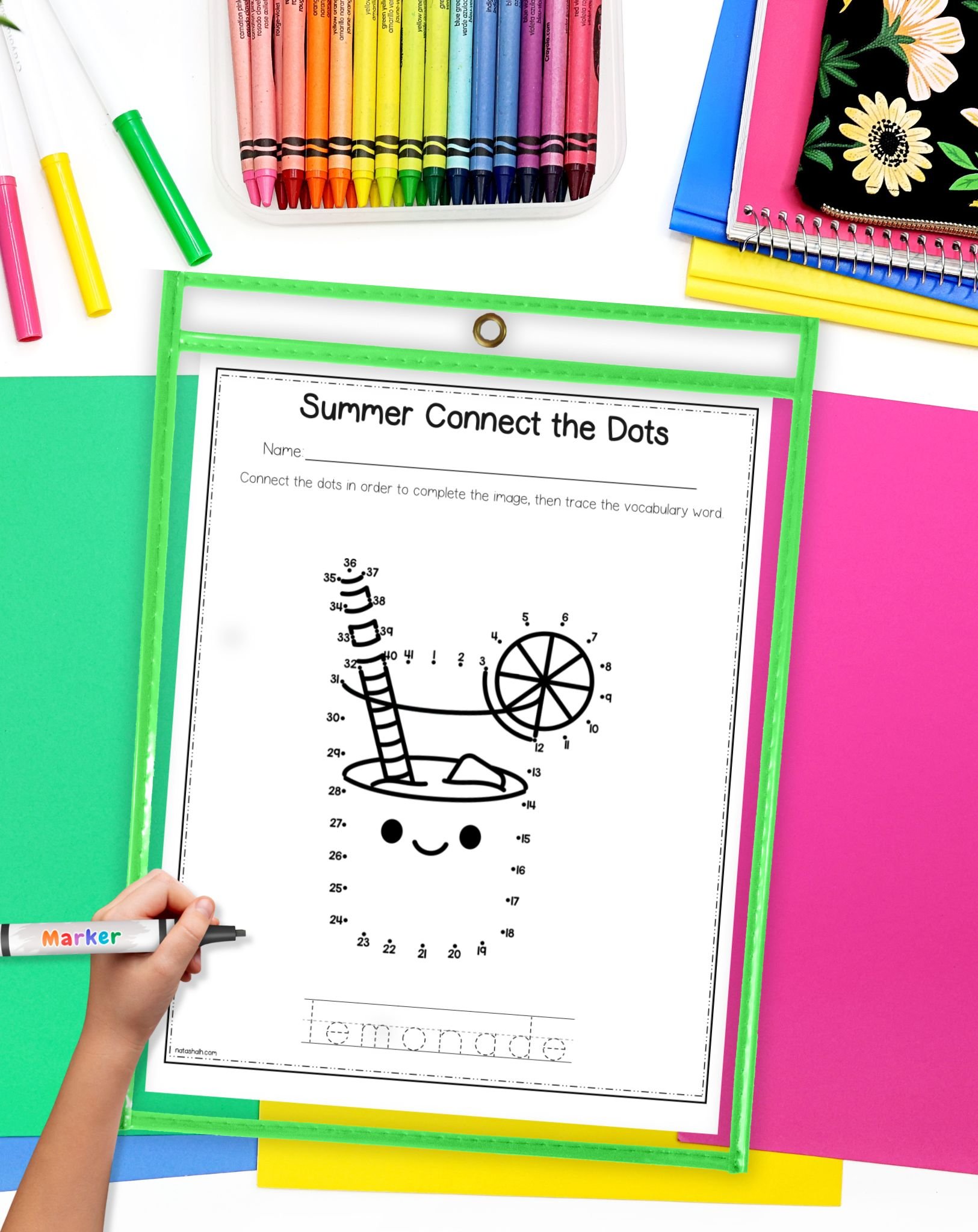 A hand is using a marker to complete a "Summer Connect the Dots" printable featuring a lemonade illustration with numbered dots, alongside colorful craft supplies on a table.

